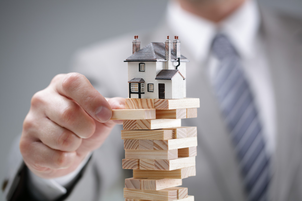 a businessman playing with a miniature house on top of stacked wooden blocks